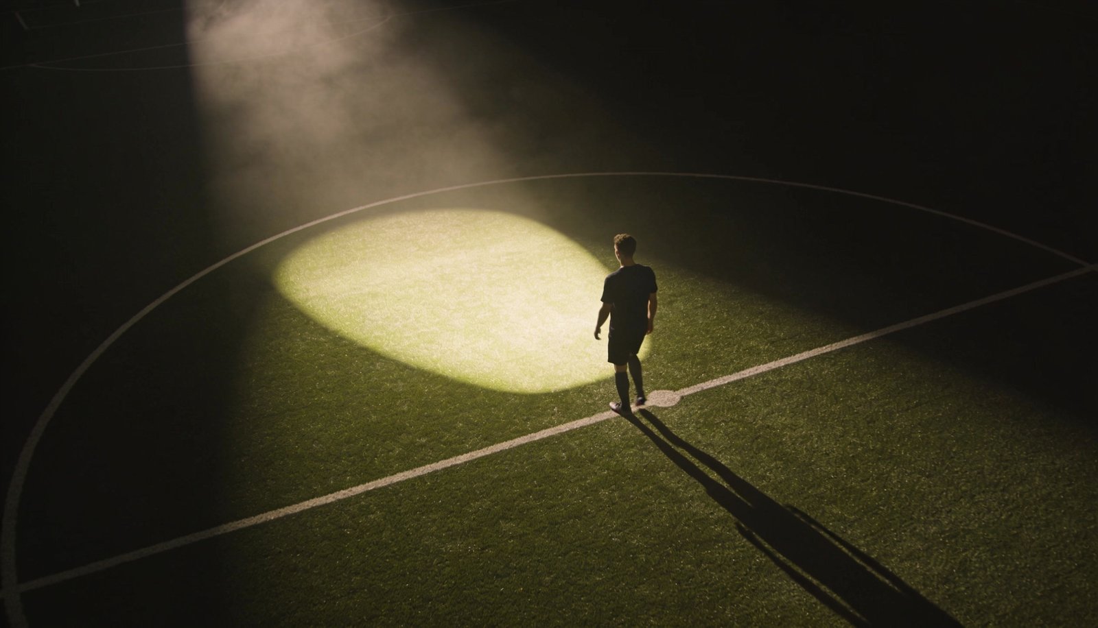 Jogador entrando sozinho em campo iluminado à noite